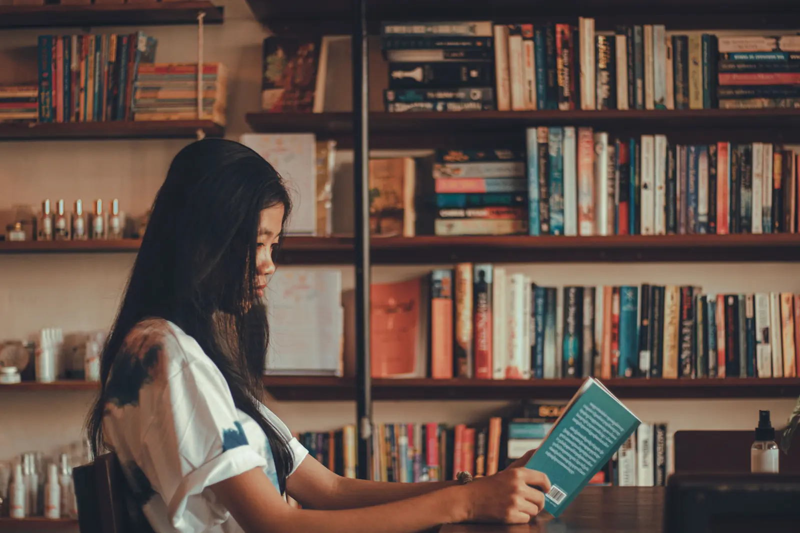 A young woman reading a book at a table in front of full bookshelves in Cambodia